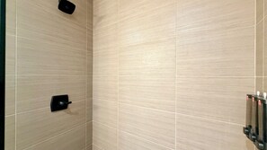 Ein Badezimmer mit hellbeige Fliesen, einem schwarzen Handtuchhalter und einer schwarzen Bedienkonsole.