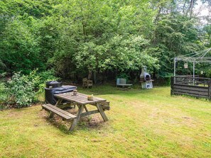 Ein Garten mit einem Holztisch, einem Grill, einer Bank und einem Pergola mit einer Laterne.