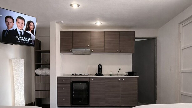Een moderne hotelkamer met kitchenette, twee bedden en een tv waarop een programma wordt vertoond.