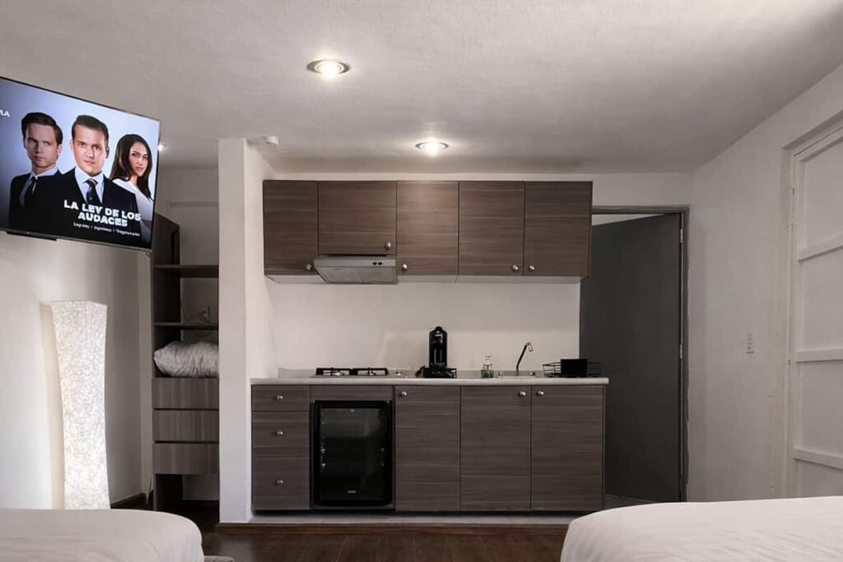 A modern hotel room with a kitchenette, two beds, and a TV displaying a show.