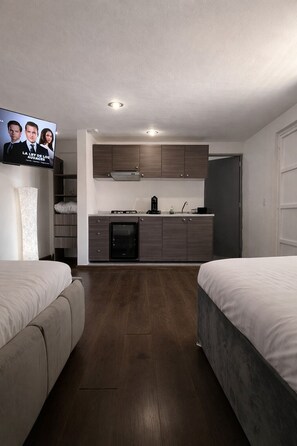A modern hotel room with a kitchenette, two beds, and a TV displaying a show. - Milan Providencia  (Guadalajara)