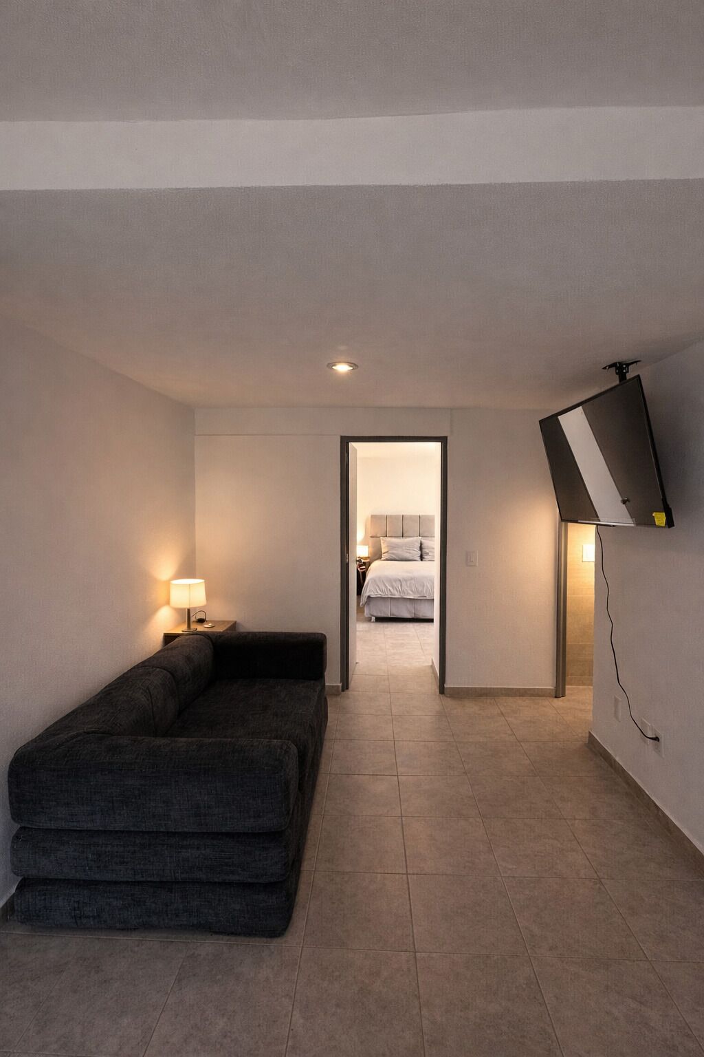 Et moderne hotelværelse med en sofa, en seng, et tv ophængt på væggen og et lille bord med en lampe.