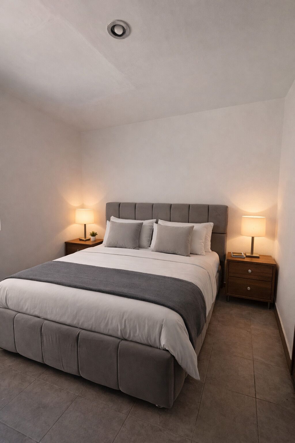 A neatly arranged bedroom with a large bed, two bedside tables, and a ceiling light.