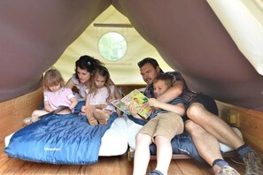 A family of five inside a tent-like room with a circular window, a blue blanket, and a pillow labeled 'Quechua'. - Camping 3 étoiles - Piscine  - ccbaefd (Grand-Laviers)
