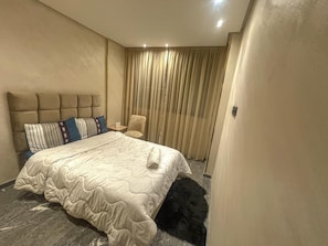 Ein Hotelzimmer mit Bett, Stuhl, kleinem Tisch und Vorhang.