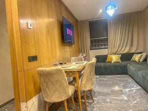 Ein modernes Wohnzimmer mit Essbereich, einer Couch, einem an der Wand befestigten Fernseher und einer Pendelleuchte.