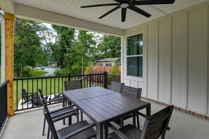 Une terrasse couverte avec une table et des chaises, un ventilateur de plafond et une vue sur un lac et des arbres.