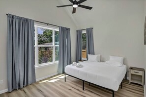Ein Schlafzimmer mit einem Bett, zwei Nachttischen, einem Deckenventilator und großen Fenstern mit Vorhängen.