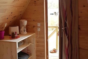 A wooden interior with a kitchenette, a wooden door, and a view of the outside.