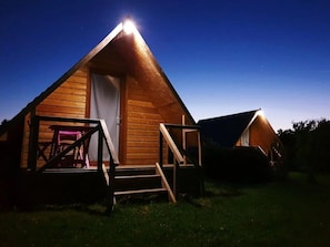 A wooden cabin with a porch and steps, a door, and a small table with chairs.