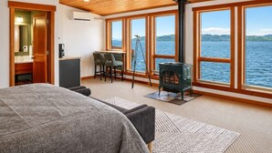 A room with a bed, a desk, a chair, a stove, and large windows overlooking a body of water. - Pier 39 Over the water full River View + Fireplace (Astoria)