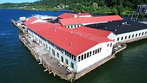 A waterfront building with a red roof, multiple windows, and a dock extending into the water. - Pier 39 Over the water full River View + Fireplace (Astoria)
