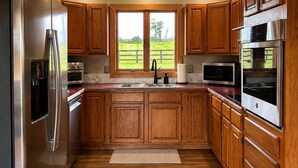 A kitchen with wooden cabinets, stainless steel appliances, a window with a view of a green landscape, and a marble backsplash. - 3br farmhouse on horse farm - close to KY Horse Park, Hagyard + Rood & Riddle (Lexington)
