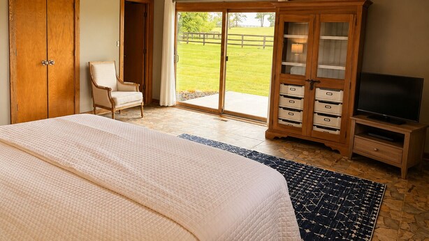 A bedroom with a bed, a chair, a TV, a wardrobe, and a sliding glass door leading to a balcony. - 3br farmhouse on horse farm - close to KY Horse Park, Hagyard + Rood & Riddle (Lexington)