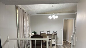 Una escalera con detalles de madera, un comedor con sillas y una mesa, y un pasillo con ventilador de techo.