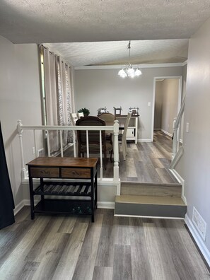 A staircase with a wooden finish, a dining area with chairs and a table, and a hallway with a ceiling fan.