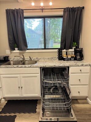 A kitchen with a dishwasher, a coffee maker, and a window with curtains.