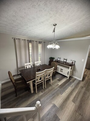 A dining area with a dark wooden table, white chairs, a chandelier, and a kitchen area with a white cabinet and a plant. - 4-bedroom welcoming getaway in Jonesboro Ga (Jonesboro)