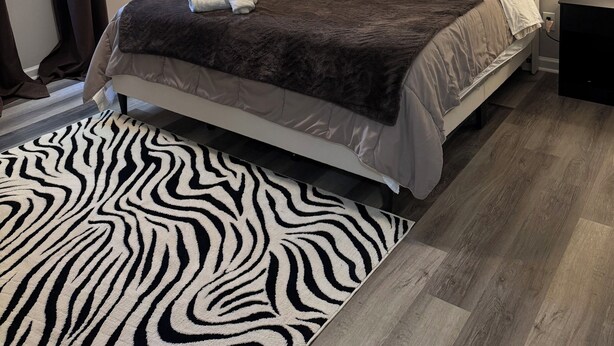Un dormitorio con cama, ventilador de techo, espejo, mesita de noche y alfombra estampada de cebra.