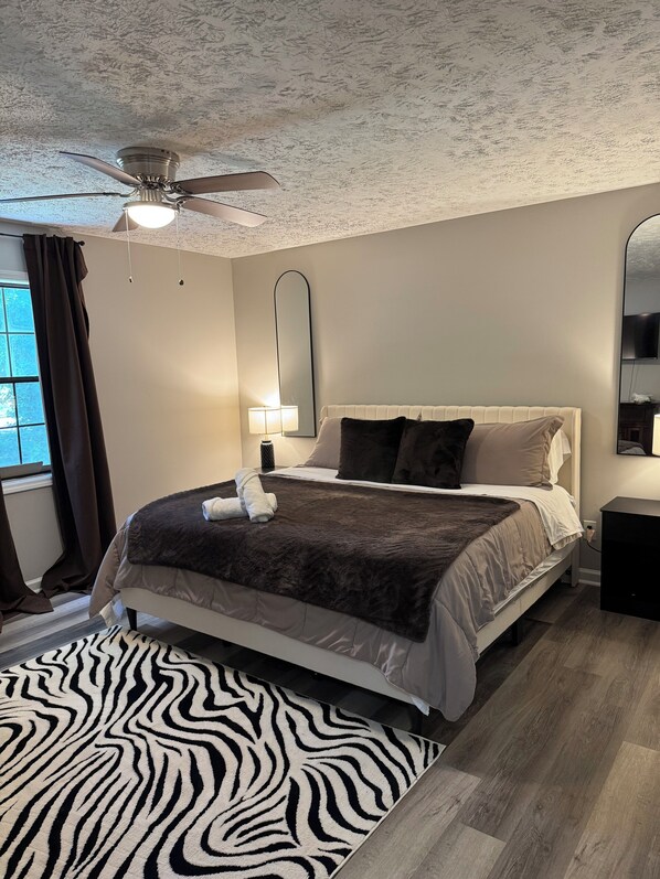 A bedroom with a bed, a ceiling fan, a mirror, a nightstand, and a zebra-patterned rug.