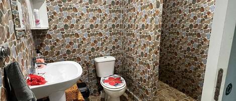 Un baño con pared de diseño de piedra, un lavamanos blanco, dos inodoros y un felpudo a rayas.