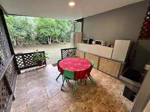 Une terrasse avec une table et des chaises, un réfrigérateur et une vue sur la verdure.