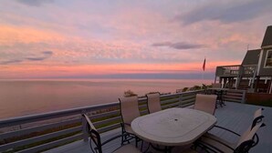 Een terras met tafel en stoelen met uitzicht op een wateroppervlak tijdens zonsondergang.