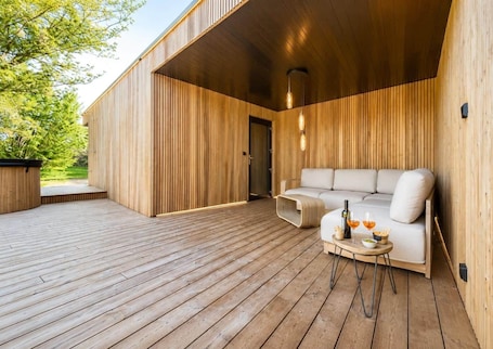 A wooden deck with a sofa and drinks, a hot tub, and a wooden wall.
