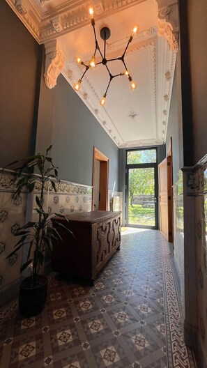 A hallway with a patterned floor, a large wooden bench, a potted plant, and a ceiling light fixture.