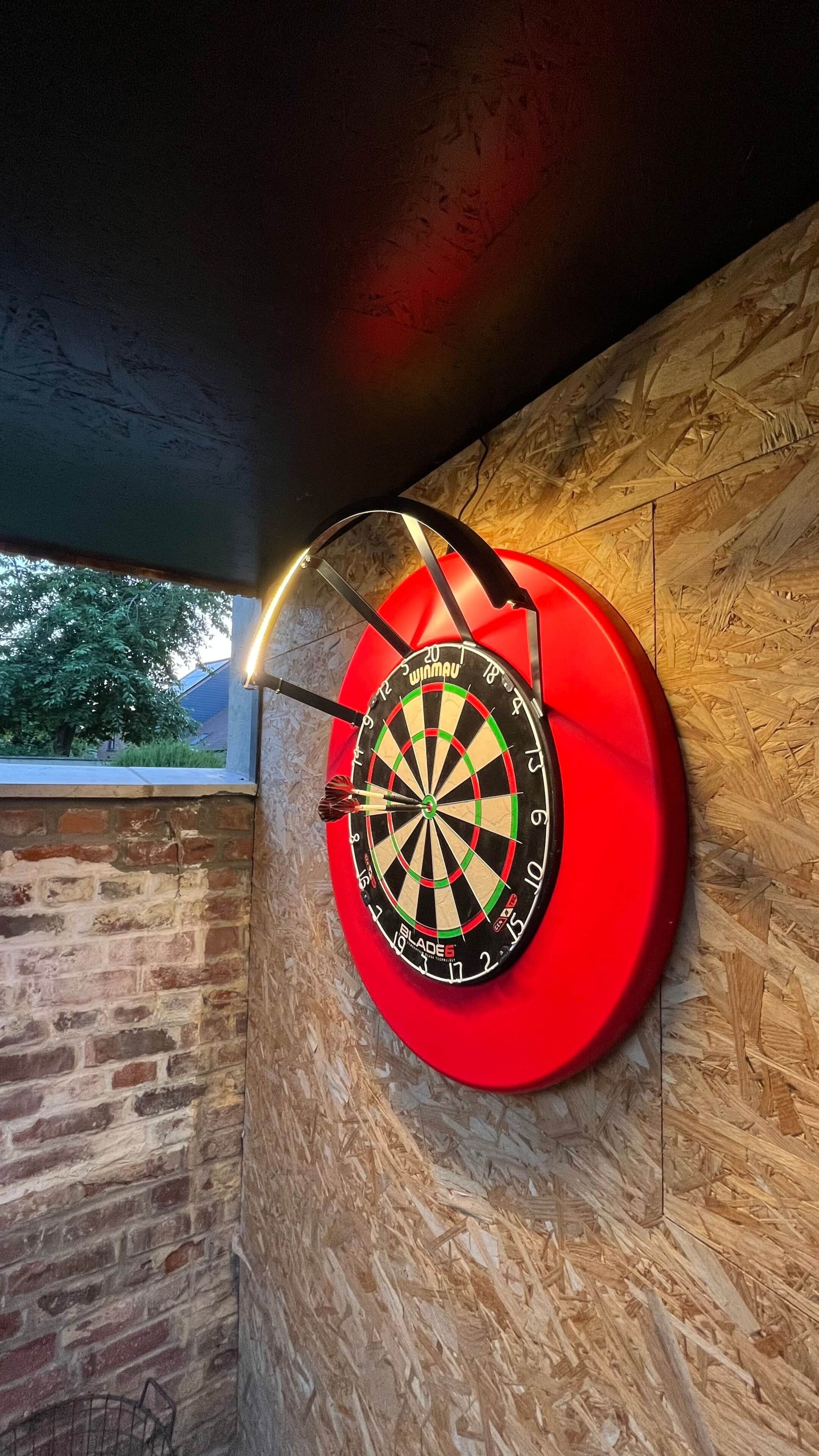 A dartboard mounted on a wooden wall with a window in the background.
