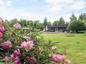 Ein modernes Haus mit Terrasse, umgeben von einer grünen Rasenfläche und blühenden rosa Blumen.