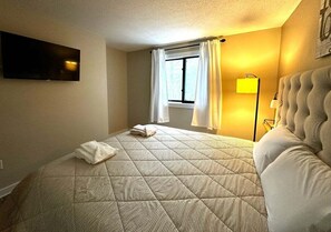 A hotel room with a bed, a flat-screen TV mounted on the wall, a window with curtains, and a bedside lamp. - Pet Friendly Waterville Valley Condo close to Town (Waterville Valley)