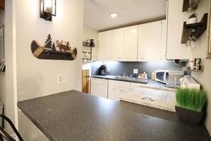 A kitchen with white cabinets, a granite countertop, a coffee maker, a microwave, and a small plant. - Pet Friendly Waterville Valley Condo close to Town (Waterville Valley)