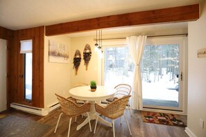 A dining area with a round table, wicker chairs, a potted plant, and a view of a snowy landscape through a glass door. - Pet Friendly Waterville Valley Condo close to Town (Waterville Valley)