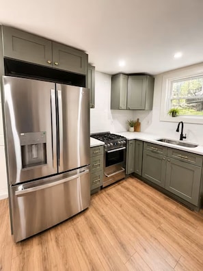 A modern kitchen with stainless steel appliances, wooden flooring, and light-colored cabinets.