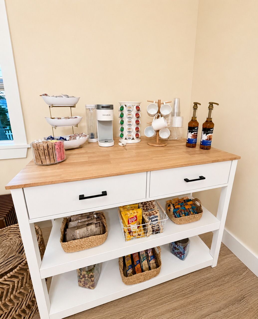 A kitchen counter with various items including a coffee maker, a kettle, a coffee press, and a bottle of syrup.