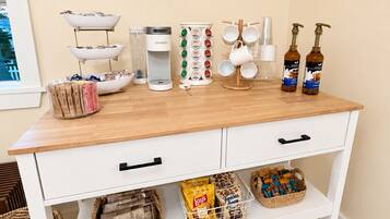 A kitchen counter with various items including a coffee maker, a kettle, a coffee press, and a bottle of syrup.