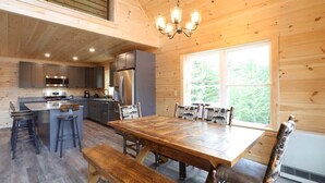Un interior de madera con cocina, mesa de comedor, taburetes de bar y un gran ventanal.