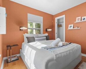 Un dormitorio con cama, ventana, puerta y estante con fotografías.