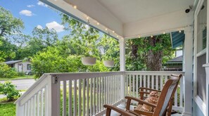 A porch with a wooden chair, a hanging light fixture, and a view of a residential street with trees. - Your E Austin Story Starts at The Bright Blue Bungalow Mins to Lady Bird Lake (Austin)
