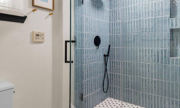 Un baño con cabina de ducha de vidrio, inodoro y panel de control en la pared.