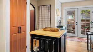 Eine Küche mit Holzarbeitsplatte, hängenden Küchenutensilien, einem Fenster mit Blick auf eine Terrasse und einer Glastür.