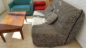 Ett vardagsrum med en turkos soffa, en röd fåtölj, en brun soffa med vita prickar och ett soffbord i trä.