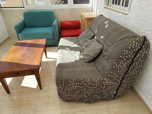 A living room with a teal sofa, a red chair, a brown sofa with white polka dots, and a wooden coffee table. - House with a pool and air conditioning (Mazarrón)