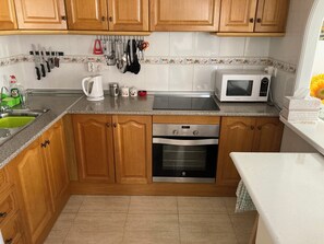 A kitchen with wooden cabinets, a stainless steel oven, a microwave, and a sink with a green dish rack. - House with a pool and air conditioning (Mazarrón)