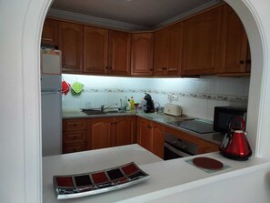 Een keuken met houten kastjes, een wit aanrecht, een spoelbak, een fornuis, een magnetron en een waterkoker.