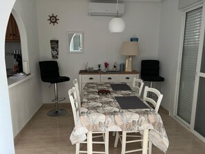 A dining area with a table set for four, a chair, a lamp, and a small cabinet. - House with a pool and air conditioning (Mazarrón)