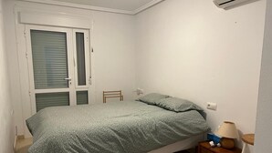 En säng med ett mönstrat överkast, ett sängbord med en lampa och en stol.