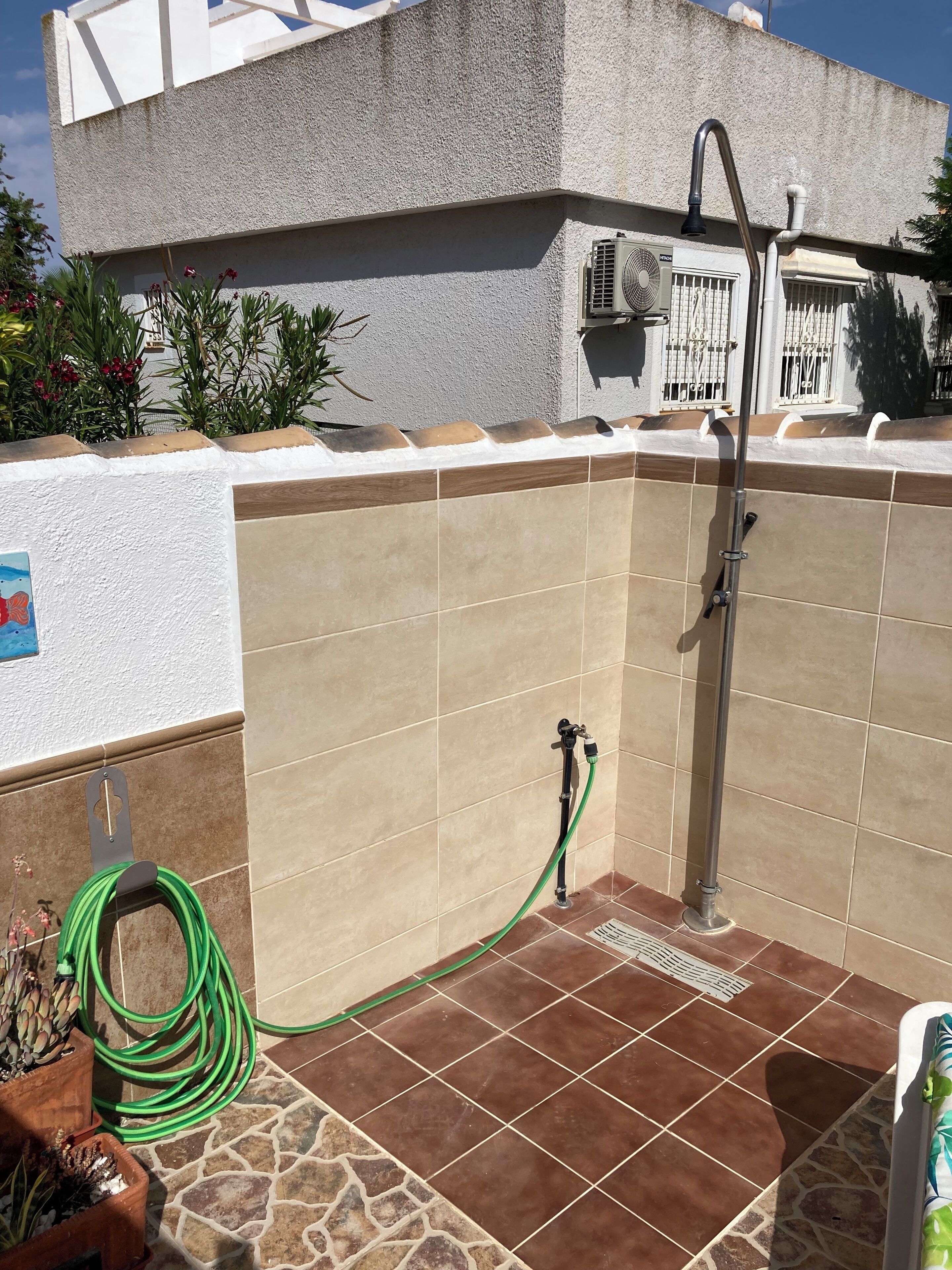 Un espace de douche extérieur carrelé, équipé d’un tuyau d’arrosage, d’un robinet en métal et d’un drain.