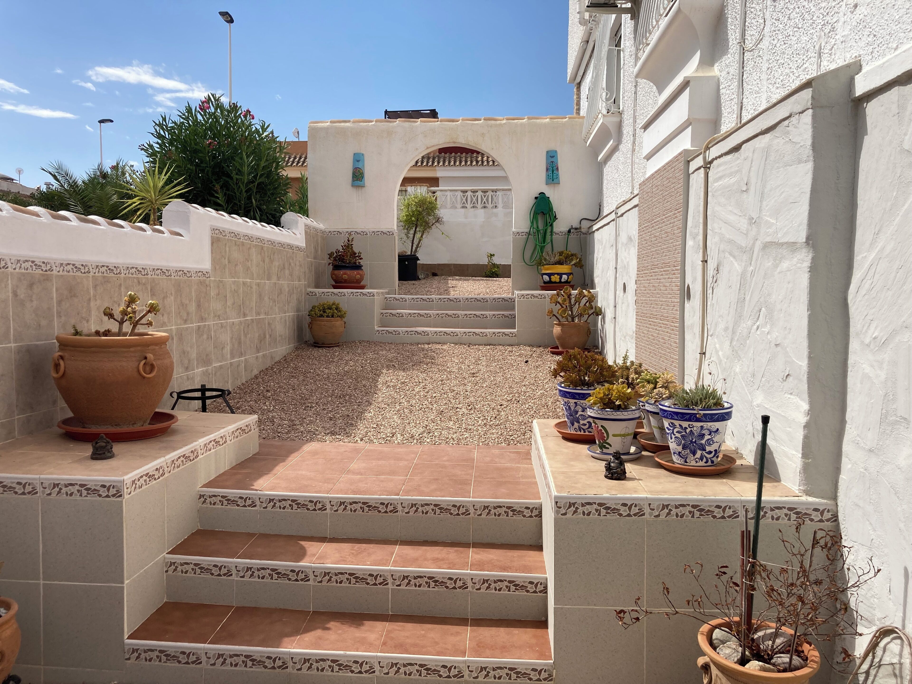 A courtyard with terracotta tiles, potted plants, and a staircase leading to a door.